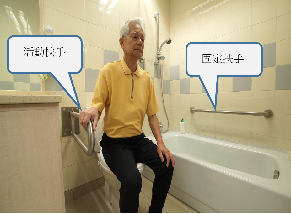 A man sitting at a toilet bowl. To assist toileting and bathing, a movable grab bar is installed to his right, and a horizontal fixed grab bar is installed to his left, by the side of the bath tub. 