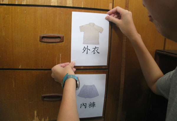 A cupboard with multiple drawers, one with a label written “outerwear” and a shirt printed, another with “underwear” and a pant printed. Both labels were affixed to the cupboard